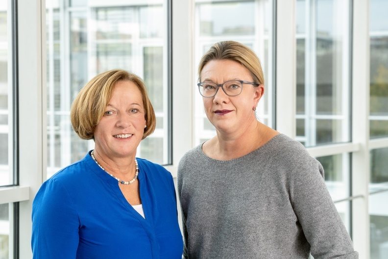 Porträt zweier Frauen vor einer Fensterfront.