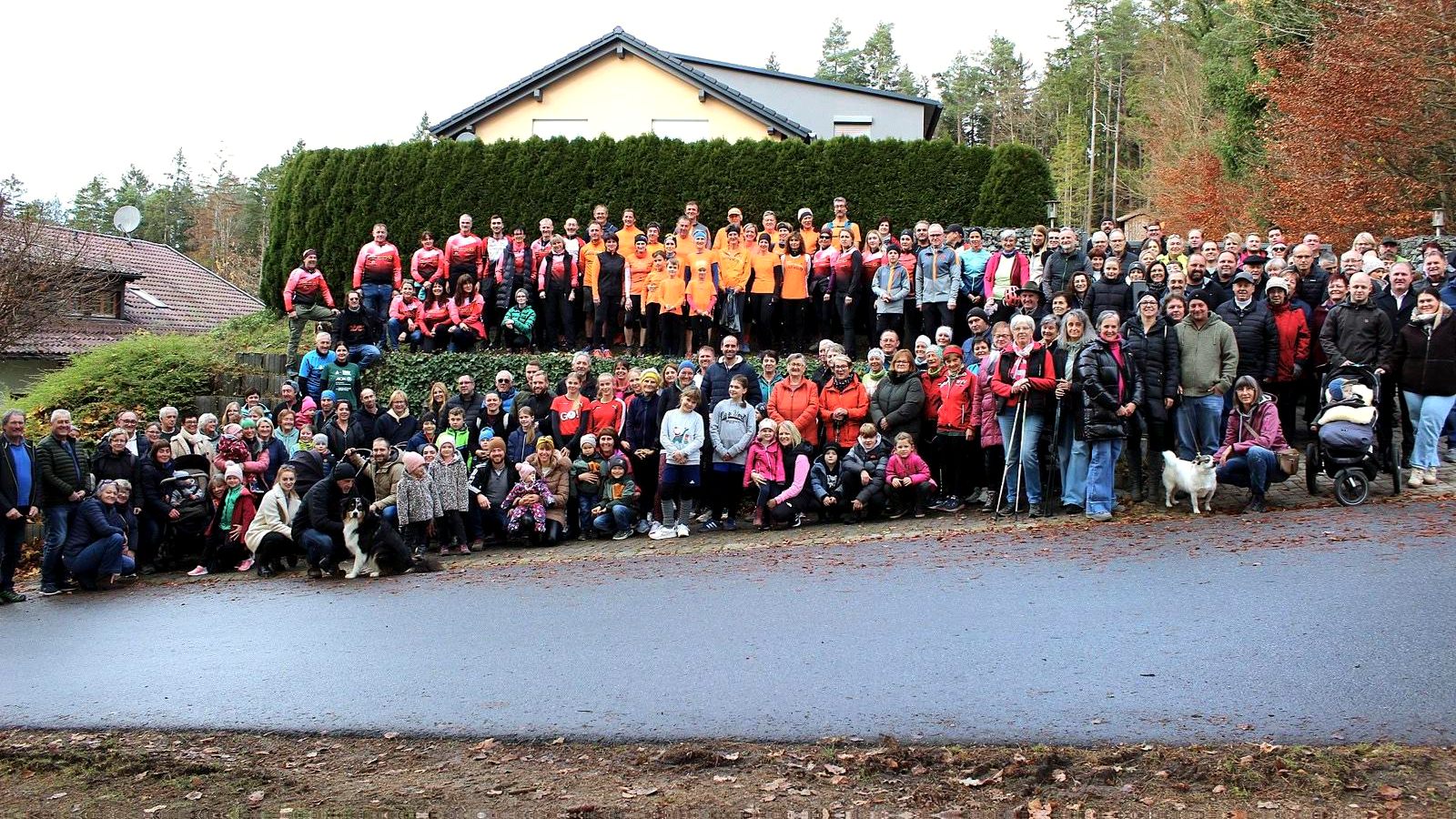 Kinderherzenlauf 2025: mehr als hundert Menschen aller Generationen, viele in orangen Shirts, beim Gruppenfoto zum Spendenfest der Familie Kirchberger.